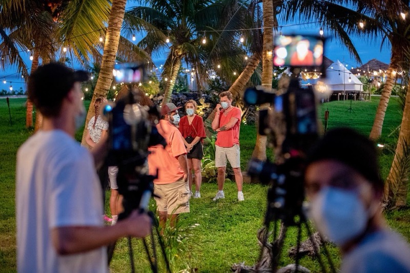 Dual-camera setup filming a reality format on the beach at dusk